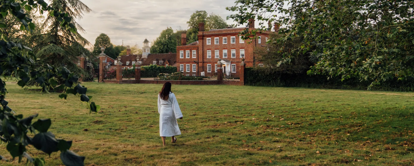 A guest in a white robe on the lawn in front of the manor at Champneys Henlow